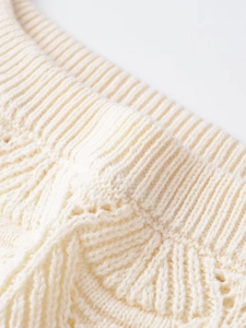 Detail of off-white knit top showing ribbed neckline and hollow crochet patterns
