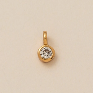 Close-up of a gold round pendant with a clear zircon stone on a beige background