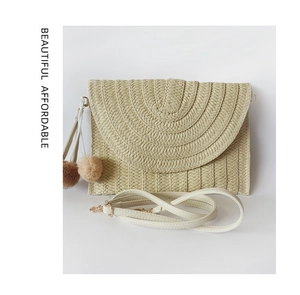 Detail view of woven straw shoulder bag with colorful pom-poms and leather strap