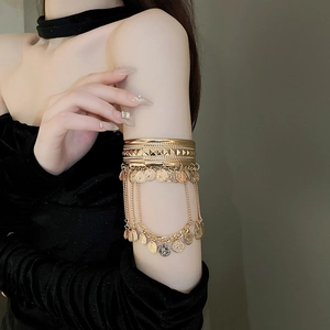 Detail of bohemian gold alloy arm cuff with layered rings and hanging coin pendants