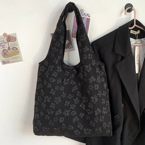 Detail of black embroidered lace floral tote bag hanging against a white wall