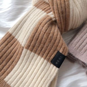 Detail of soft checkered knit scarf in beige and brown with woven brand label
