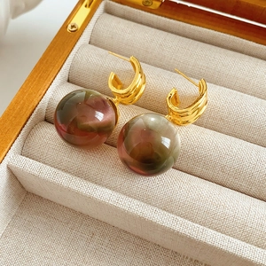 Close-up of gold U-shaped earrings with red and green gradient resin sphere pendants