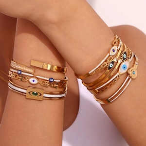 Close-up of stacked 18K gold-plated bracelets featuring evil eye charms and zircons