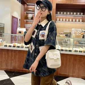 Detail of white canvas crossbody bag with bow appliqué worn with camo bear print shirt