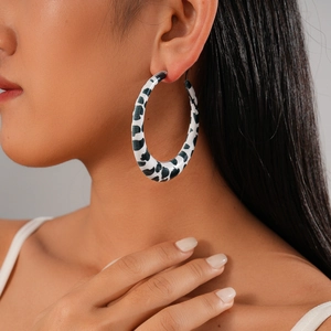 Macro detail of large black and white cow print hoop earring worn by a model