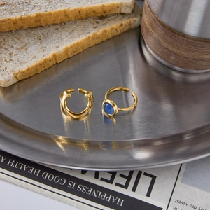 Detail of gold U-shaped open ring and blue gemstone ring set on a brushed steel tray