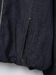 Detail of dark blue denim bomber jacket showing white contrast stitching and metal zipper