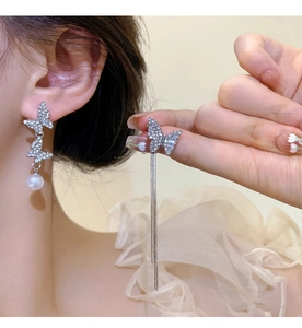 Detail of silver bow earrings with sparkling crystals, long tassels and white pearls