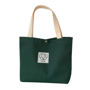 Green canvas tote bag with cream handles and cute dog patch at a 45-degree angle