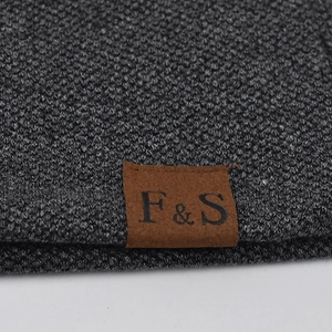 Detail of dark gray knit beanie fabric with brown leather patch and embossed logo