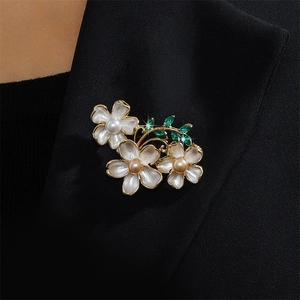 Elegant enamel flower brooch with pearls and green gems on a black suit lapel