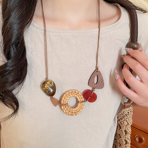 Detail of bohemian necklace with woven straw circle and amber resin pendant on a model
