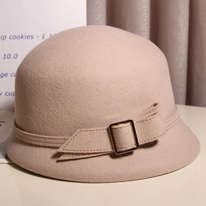 Détail d'un chapeau cloche en laine beige montrant le nœud et la boucle en métal doré