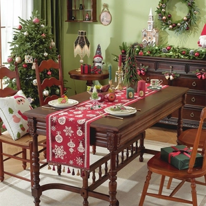 Red Christmas table runner with white snowflakes and tassels on dark wooden table