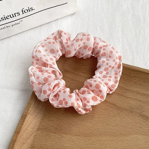 Detail of light pink floral scrunchie with orange polka dots on a wooden tray