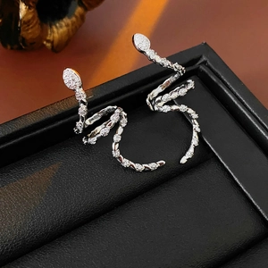 Macro shot of silver snake-shaped earrings with clear zircon stones on black leather