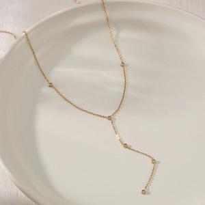 Minimalist gold Y-shaped stainless steel necklace with sparkling zircon tassels in ceramic tray