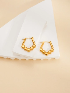Detailed view of gold beaded horseshoe earrings on a white stone display platform