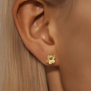 Detailed view of flower stud earring with gold petals and a purple center gemstone