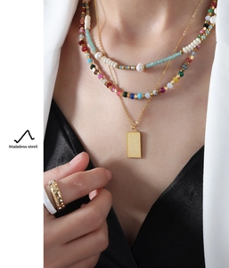 Detail of layered stainless steel necklaces with colorful tourmaline and gold pendants