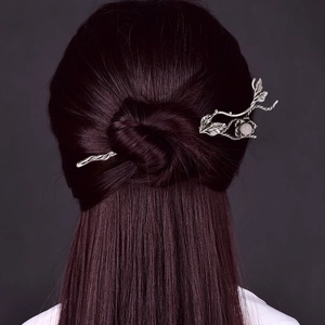 Elegant metallic hair stick with leaf design and white gemstone in a sleek bun hairstyle
