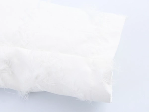 Dettaglio del tessuto bianco strutturato con bordi a frange su un cappotto lungo