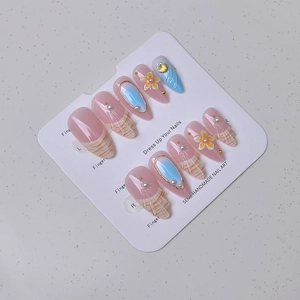 Detail of almond press-on nails with 3D flowers, gold shells, and pearls on card