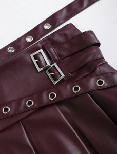Detail of burgundy PU leather pleated skirt with silver metal buckles and eyelets