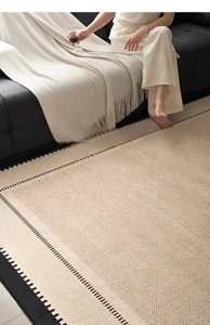 Detail of retro woven rug with black border on light wood floor next to a leather sofa