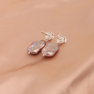 Detail of baroque pearl earrings with silver rose design on champagne satin fabric
