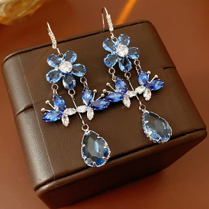 Close-up of blue crystal flower and teardrop tassel earrings on leather jewelry box