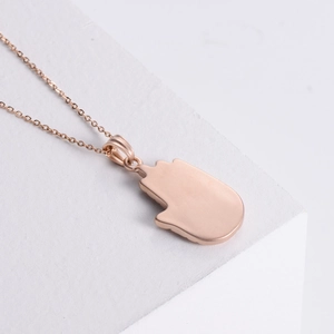 Rose gold Hamsa Hand pendant necklace on white stones with a 45-degree angle view