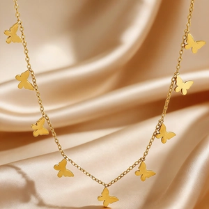 Detail of gold butterfly charms on thin chain necklace over champagne silk background