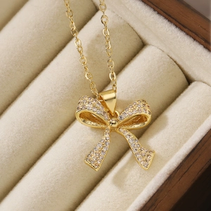 Elegant gold bow pendant necklace with sparkling cubic zirconia on a beige jewelry box