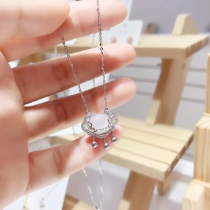 Close-up of silver Ruyi lock necklace with white gemstone held by hand against wood