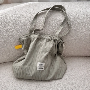 Detail of grey pleated tote bag with yellow side strap and textile label on white sofa