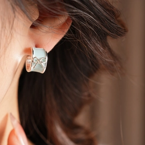 Close-up of a blue enamel C-shaped earring with a silver bow knot on a model's ear