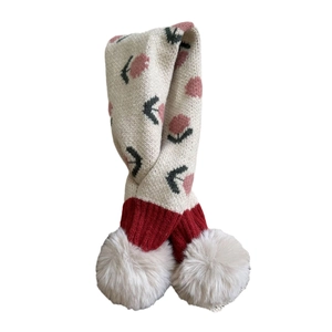Winter knit children scarf with floral pattern and soft white pom-poms on plain background