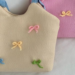 Detailed view of woven straw bags with colorful handmade crochet bows on white fabric