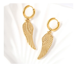 Détail de boucles d'oreilles ailes dorées montrant la texture fine des plumes sur coquillage