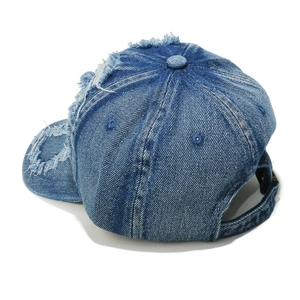 Detail of distressed denim baseball cap showing frayed holes and washed blue fabric