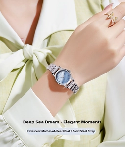 Detalle de reloj de acero plateado con esfera de nácar azul y un anillo de mariposa dorado