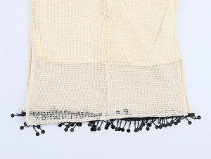 Detail von beige Häkel-Netzstoff mit dekorativen schwarzen Quasten am Saum des Kleides