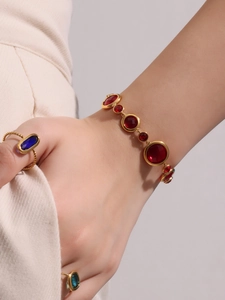 Detail shot of a model wearing a luxury gold bracelet with red stones and blue vintage rings