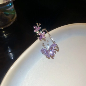 Macro shot of silver butterfly ear cuffs with purple crystals on a ceramic edge
