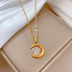 Detail of moon and white rabbit pendant on gold chain necklace over beige padding