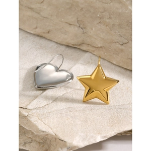 Detail of asymmetric earrings with a silver heart and gold star on a stone background