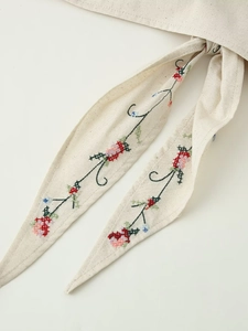 Détail de la broderie florale sur un haut dos nu en lin beige avec liens à nouer