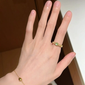 Detailed view of textured gold ring with green gemstone and heart pendant bracelet